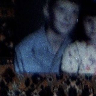Woman sits on a patterned couch with a portrait above.