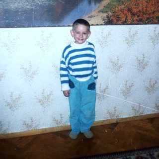Boy stands before a landscape photograph on a textured wall.
