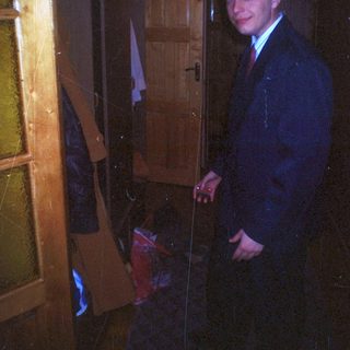 Man in suit stands in a doorway, dimly lit room.