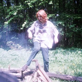 Person balances on logs in a wooded area.