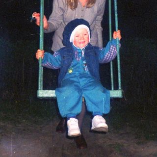 Girl and child on a swing set at night.