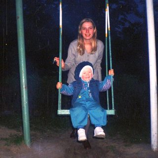 Girl and child on a swing set at night.