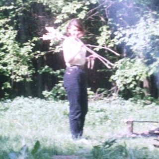 Person standing near a campfire in a wooded area.