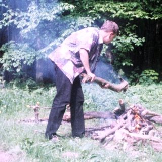 Man tending a fire in a wooded area.