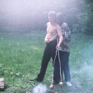 People cooking food over a fire in a wooded area.