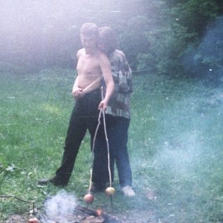 People cooking food over a fire in a wooded area.