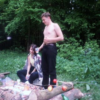 Three people relax outdoors amongst foliage and discarded items.