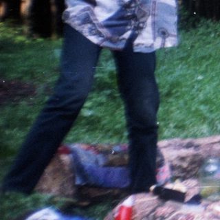 Three people relax outdoors amongst foliage and discarded items.