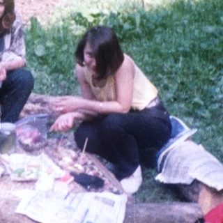 Three people relaxing outdoors on logs in a wooded area.