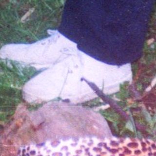 A person bends down in grass, holding a twig.