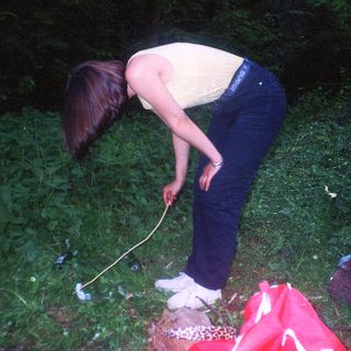 A person bends down in grass, holding a twig.