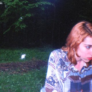 Two people near a fire in a dark, wooded area.