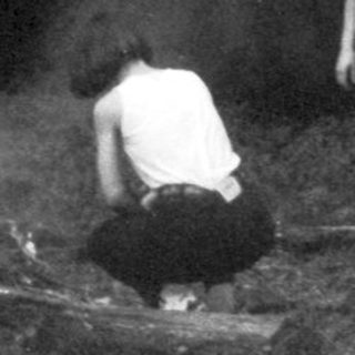 Two people near a fire in a dark, wooded area.