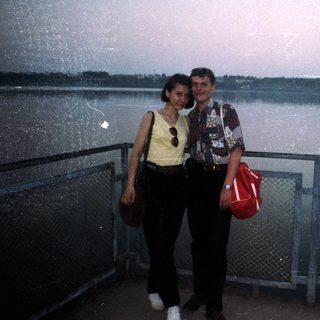 Couple poses by water with cityscape in the background.