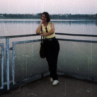 Woman stands near water, looking out at a landscape.