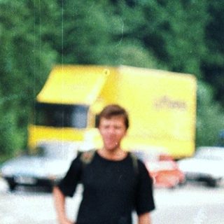 Man stands near a road under a tree canopy.