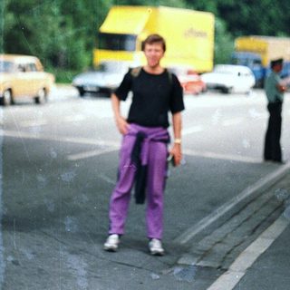 Man stands near a road under a tree canopy.