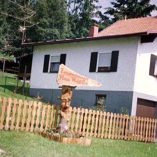 House with sign, wooden fence, and lush greenery.