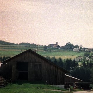 Rural village with wooden structures and a distant church.
