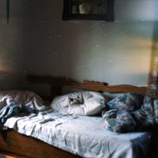Disheveled bed in a dimly lit, rustic room.