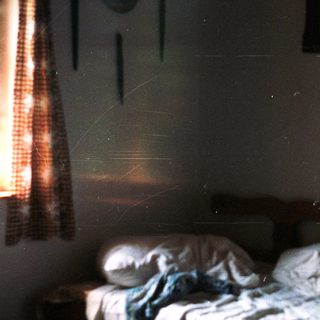 Disheveled bed in a dimly lit, rustic room.