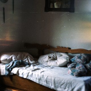 Disheveled bed in a dimly lit, rustic room.