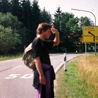 Person stands near road sign in a rural, wooded area.