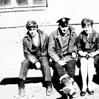 Group of people seated outdoors, possibly in a uniform.