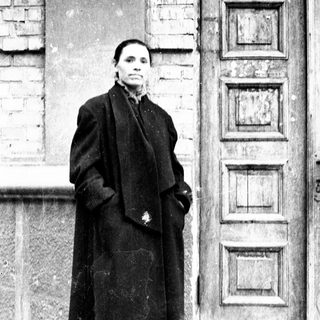 Woman stands outside a building, wearing a long coat.