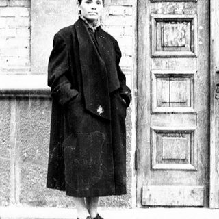 Woman stands outside a building, wearing a long coat.