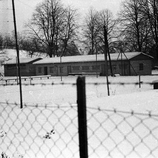 Snow-covered building with bare trees and a fence.