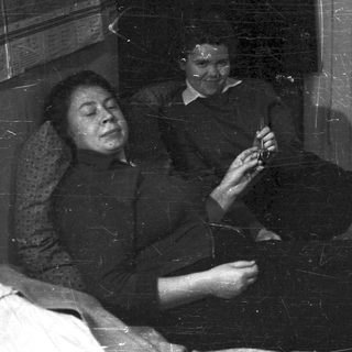 Man in suit holding object, woman seated in room.