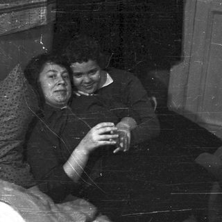 Here's a brief summary of the image: Two people sit close, smiling in a room.