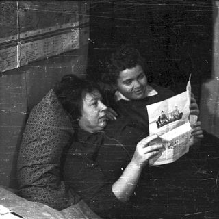 Here's a brief summary of the image: Two people examining a photograph together indoors.