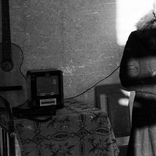 Here's a brief summary of the image: Woman stands in a room with strong light and shadows.