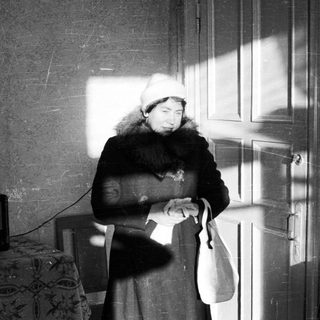 Here's a brief summary of the image: Woman stands in a room with strong light and shadows.