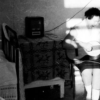 Here's a brief summary of the image: Person playing guitar, seated in a room with light.