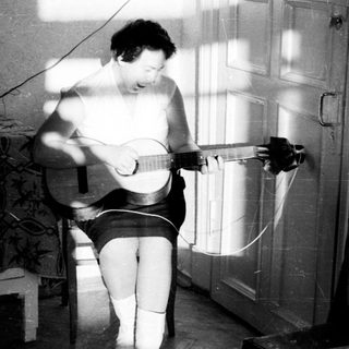 Here's a brief summary of the image: Person playing guitar, seated in a room with light.