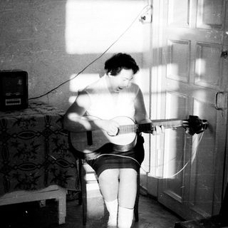 Here's a brief summary of the image: Person playing guitar, seated in a room with light.