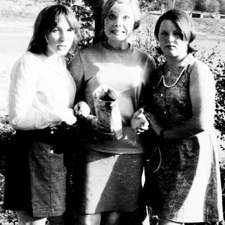 Three women posing outdoors, holding a small object.