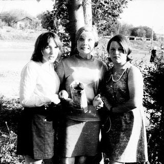 Three women posing outdoors, holding a small object.