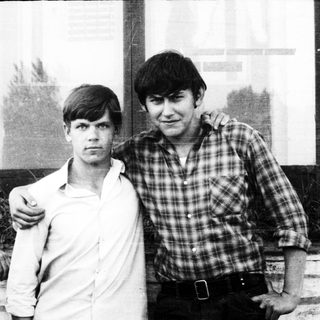 Two young men standing together outdoors, casually posed.