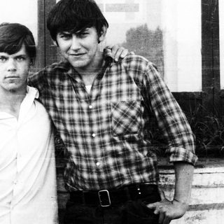 Two young men standing together outdoors, casually posed.