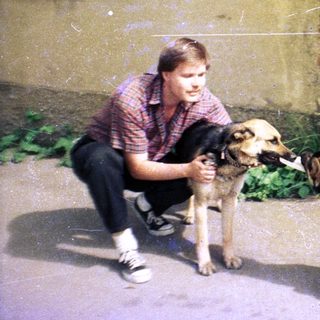 Man crouches, interacting with three dogs near a building.
