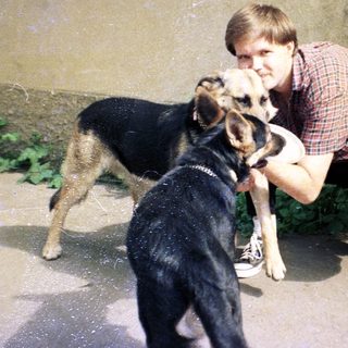 Man crouches, petting a dog outside a building.