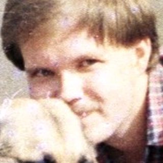 Man crouches, petting a dog outside a building.