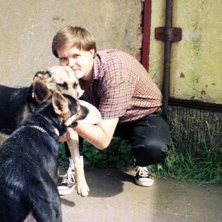 Man crouches, petting a dog outside a building.