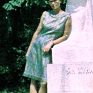 Woman stands near a statue in an outdoor setting.
