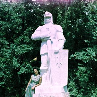 Woman stands near a statue in an outdoor setting.