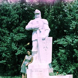 Woman stands near a statue in an outdoor setting.